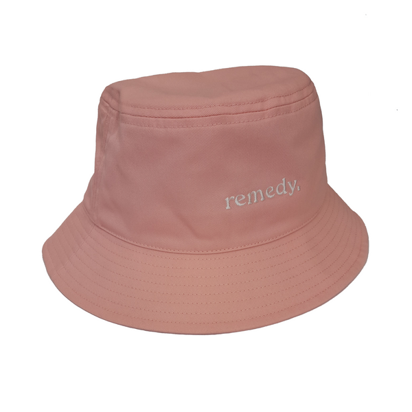 A side view of pink bucket hat with white embroidery branded 'remedy' on the front.