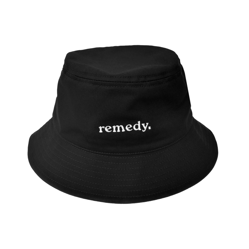 A front view of black bucket hat with white embroidery branded 'remedy' on the front.